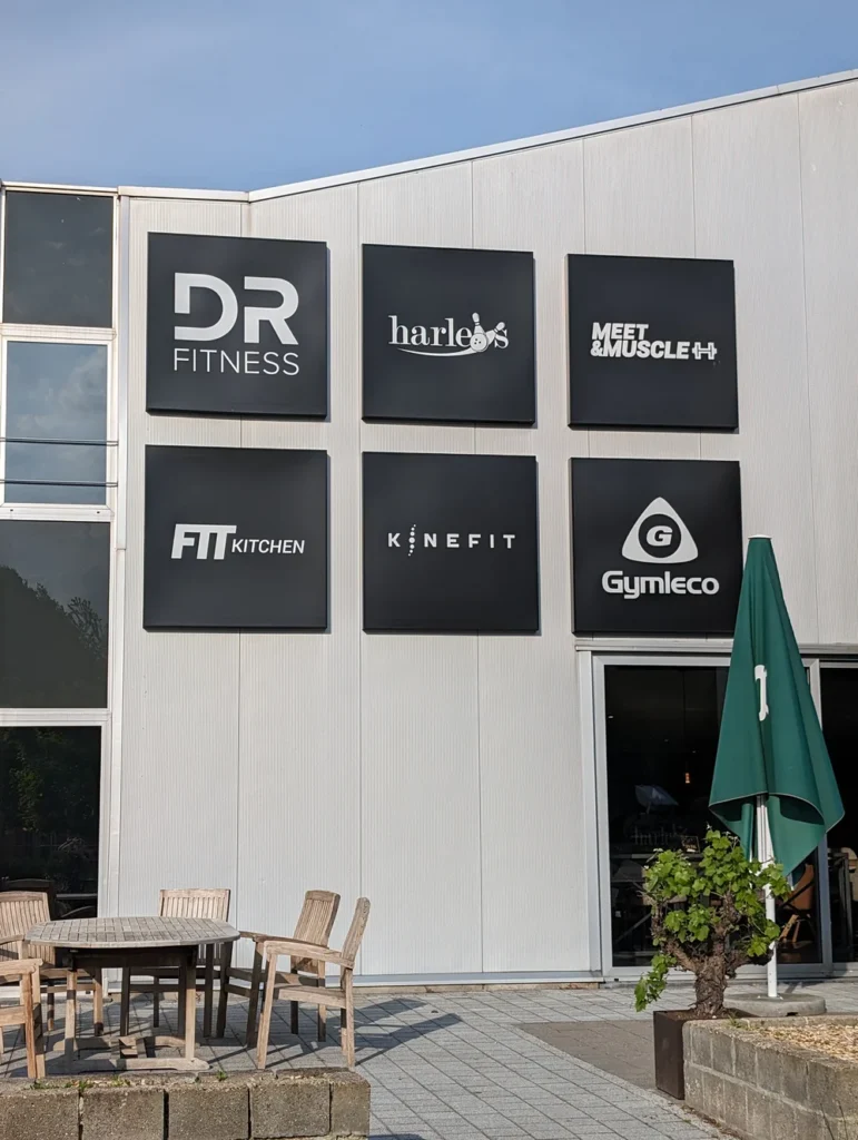 Wit Kinefit-logo op een zwart paneel aan de gevel van de vroegere Fitlounge in Meeuwen (Oudsbergen)
